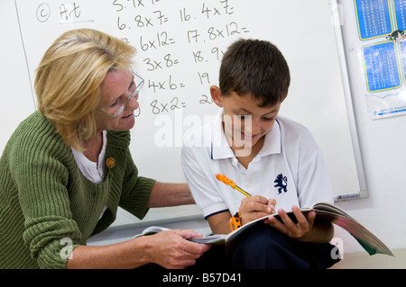 Maths Teacher e Junior School boy 7-10 anni e lavagna bianca che lavora su tabelle di tempo con somme matematiche con l'aiuto di un'insegnante femminile in classe scolastica Foto Stock