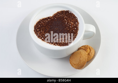 Tazza di caffè bianco con un cuore di cioccolato modellato agitare topping e due amaretti sul lato. Foto Stock