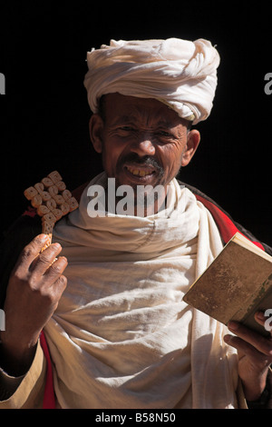 Sacerdote tiene croce e la bibbia al di fuori di due chiese gemelle di Bet Golgota e scommettere Mikael e Selassie Cappella, Lalibela, Etiopia Foto Stock