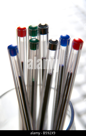 Penne colorate disposte verticalmente in un contenitore di vetro trasparente su uno sfondo luminoso Foto Stock