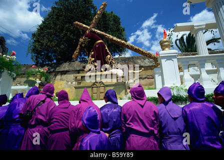 Gli uomini nelle vesti di porpora che trasportano enormi galleggiare su una delle famose processioni di Pasqua, Antigua, Guatemala, America Centrale Foto Stock