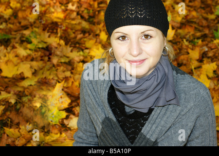 Giovane donna seduta in un parco circondato da foglie di glden Foto Stock