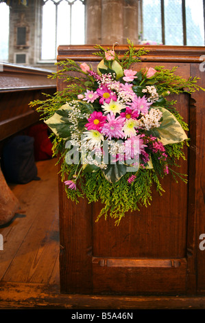 Un colorato bouquet di fiori sul lato di un pew per la celebrazione di un matrimonio in una chiesa. Foto Stock