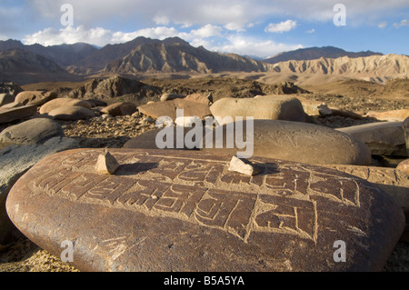 Close up tradizionale preghiera intagliato pietre su una parete di preghiera con il paesaggio del deserto e delle montagne al di là, Alchi, Ladakh, India Foto Stock