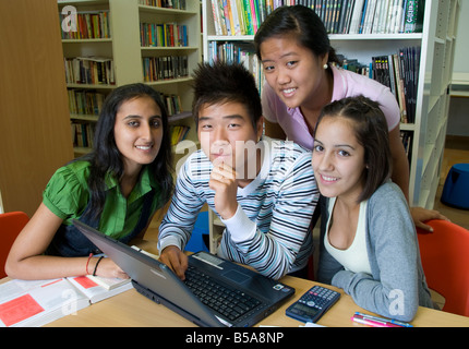 Gruppo di studio di Felice senior Asian coreano e ispanica studenti adolescenti sta lavorando a un progetto insieme su un computer portatile nella scuola della libreria di riferimento Foto Stock