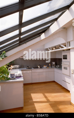 Pavimento in legno compatto bianco moderna cucina loft con montati a parete doppia forno e pendenza del tetto in vetro Foto Stock
