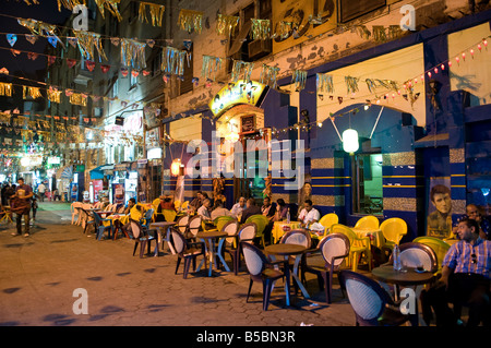 Una strada ricca di caffetterie e ristoranti con persone sedute a tavoli fuori in centro cittadino del Cairo in Egitto Foto Stock