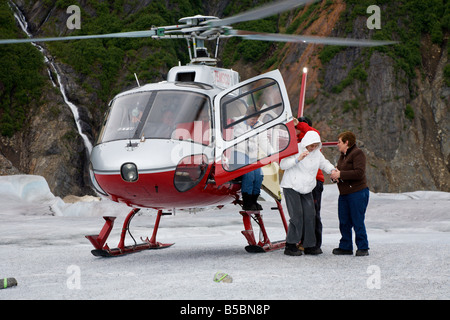 Il pilota e l'equipaggio dell'elicottero aiutano i turisti a scendere dall'elicottero sulla cima del ghiacciaio Mendenhall vicino a Juneau in Alaska Foto Stock