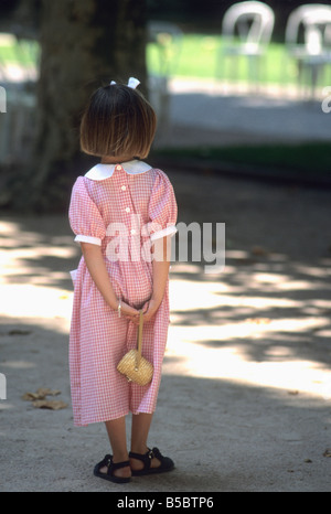 Bambina in un bel rosso vestito controllati e archetto in i suoi capelli in un parco Foto Stock