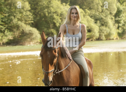 Donna bionda seduta a cavallo in un poco profondo riverbed Foto Stock