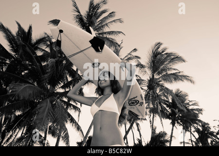 Una bella diciannovenne donna in un bikini bianco contiene una tavola da surf in Lahaina, Maui, Hawaii. Foto Stock