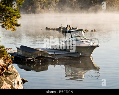 Un'imbarcazione attraccata ad una banchina coperto di brina con una nebbia rising l'acqua dietro di esso. Foto Stock