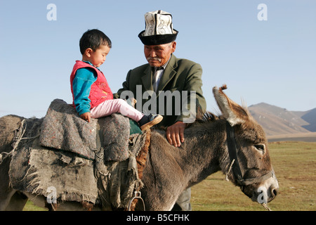 Il vecchio uomo del Kirghizistan indossando il tradizionale kalpak (HAT) e ragazzo seduto su donkey, lago Song-Kol, Kirghizistan, Asia centrale Foto Stock