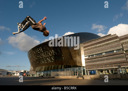 Ragazzo adolescente sumersault eseguire acrobazie su pogo rimbalzanti palafitte fuori del Wales Millennium Centre Cardiff Regno Unito Foto Stock