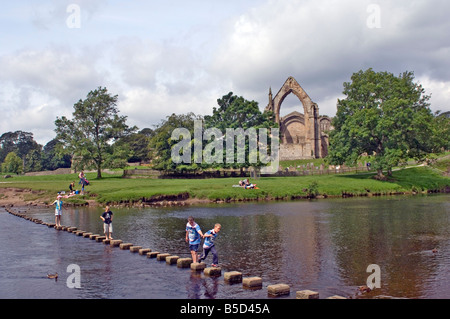 I bambini attraversando le pietre miliari attraverso il fiume Wharfe a Bolton Abbey, Wharfedale, nello Yorkshire, Inghilterra Foto Stock