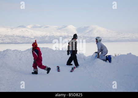 Tre bambini che giocano nella neve sopra il ghiaccio coperto lago Tornetrask, Lapponia, Svezia Foto Stock