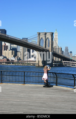 Una giovane ragazza guardando il centro di Manhattan e il Ponte di Brooklyn attraverso un gettone view finder. Foto Stock