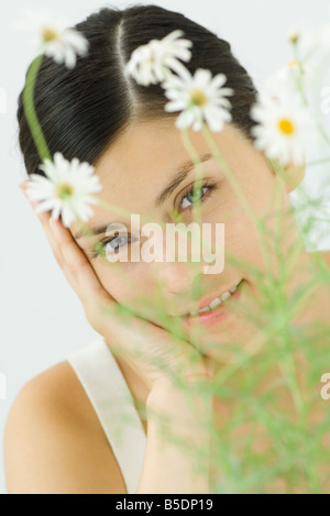 Donna che guarda la telecamera attraverso foglie della pianta di camomilla Foto Stock