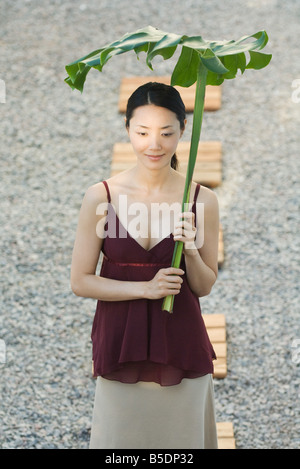 Donna che cammina nel giardino di roccia, azienda palm frond sopra la testa Foto Stock