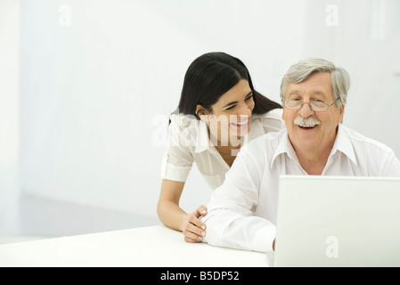 Senior uomo e metà donna adulta guardando insieme per laptop, sorridente Foto Stock