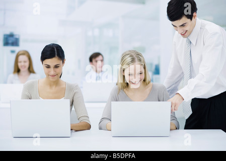 Femmina di lavoratore di ufficio con computer portatile, supervisore maschio guardando sopra la sua spalla e puntamento Foto Stock