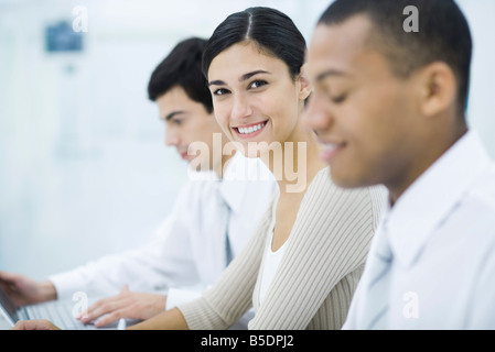 Giovani professionisti donna seduta tra due colleghi di sesso maschile, sorridente in telecamera Foto Stock