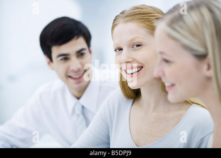 Giovane donna professionale tra due colleghi, sorridente in telecamera Foto Stock