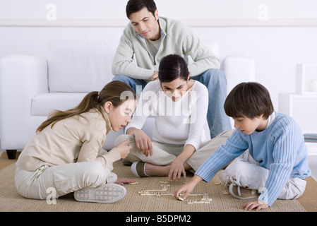 Famiglia di trascorrere del tempo insieme, madre e figli giocare domino, padre guardando Foto Stock