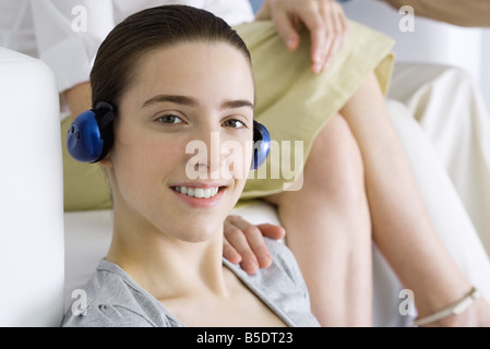 Ragazza adolescente ascoltando le cuffie, sorridente alla fotocamera, donna di mano sulla sua spalla Foto Stock