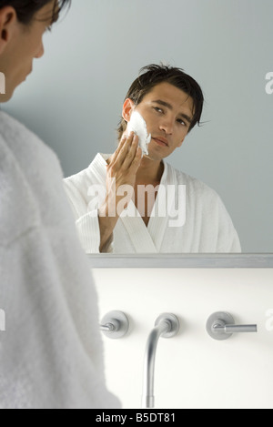 Uomo che guarda a se stesso in uno specchio, l'applicazione di crema per la rasatura Foto Stock