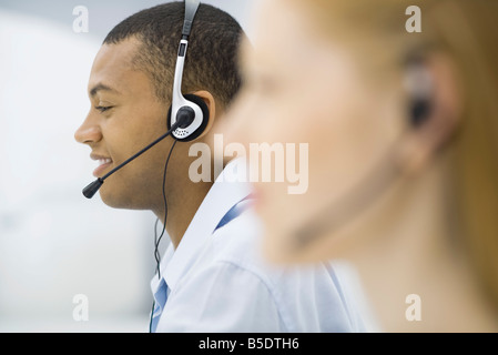 Telemarketers indossa gli auricolari, profilo, concentrarsi sullo sfondo Foto Stock