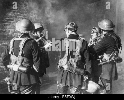 Vigili del fuoco controllare i loro apparecchi respiratori e maschere antigas prima di trasferirsi in un edificio in fiamme per affrontare un immenso incendio dopo il pesante bombardamento nel blitz durante la Seconda Guerra Mondiale;Novembre 1940 Foto Stock