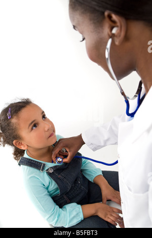 Una donna africana di medico americano utilizzando il suo stetoscopio per esaminare una razza mista bambina Foto Stock