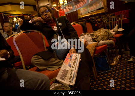 Stanco afro-americano di lady ascolta con sleeping figlia a ultime notizie durante tutta la notte notte elettorale di Londra Foto Stock