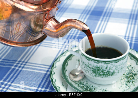 Versare fuori di riempire un bicchiere con un fresco e caldo caffè nero da un vecchio svedese POT del caffè realizzato in rame Foto Stock