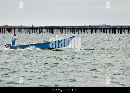 Un pescatore prende il suo giro in barca sul Bassin de Thau con i banchi di ostriche in background. Foto Stock