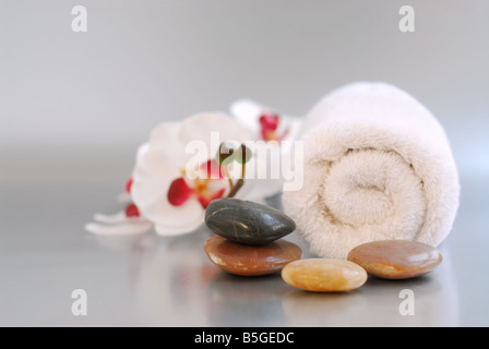 White arrotolato asciugamano massaggio con pietre e un'orchidea Foto Stock