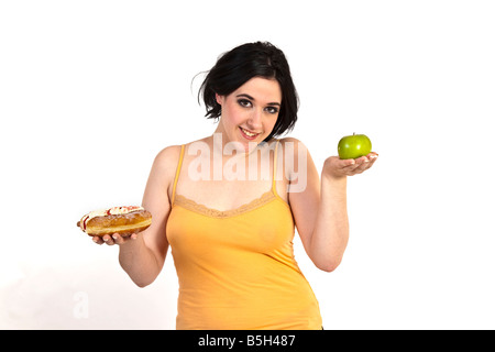 Una giovane donna cerca di decidere tra un sano apple e una malsana ciambella. Foto Stock