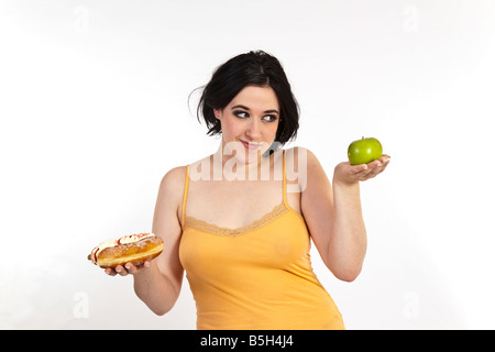 Una giovane donna cerca di decidere tra un sano apple e una malsana ciambella. Foto Stock