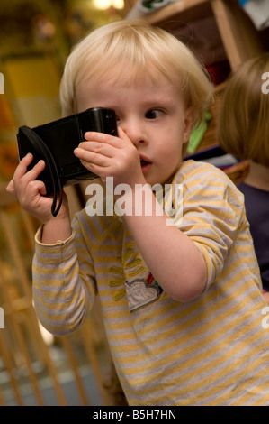 Ragazzo giovane bambino toddler in vivaio centro per la cura giornaliera del bambino guardando attraverso la vecchia macchina fotografica a giocare a essere un fotografo, REGNO UNITO Foto Stock