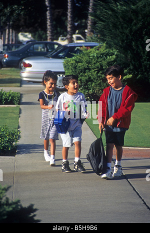 Tre bambini a piedi sul marciapiede come il loro ritorno a casa da scuola. Foto Stock