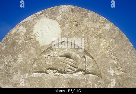 Pietra tombale sotto il cielo blu con scolpito a mano maschile raggiungendo fuori e tenendo premuto o agitando la mano femminile nel dolce ricordo Foto Stock