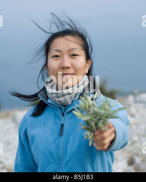 Giovane donna asiatica vestita di azzurro offre un mazzetto di appena raccolto salvia. Foto Stock