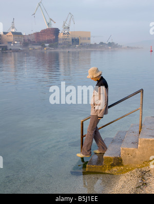 Persona in un cappello a piedi giù per le scale che portano ad acqua con cantiere in background Foto Stock