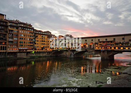 FIRENZE, Italia - lo storico Ponte Vecchio si estende sul placido fiume Arno nella luce soffusa della mattina presto. Il ponte medievale, fiancheggiato da botteghe orafe coperte, si riflette nelle acque calme sottostanti, creando una scena serena nel cuore di Firenze prima che la città si svegli. Foto Stock