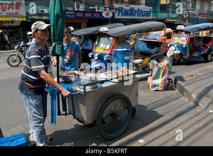 Un venditore ambulante imposta il suo mobile cucina di strada di fronte quattro tuk tuk a tre ruote rickshaws su una strada trafficata Bangkok in Thailandia Foto Stock
