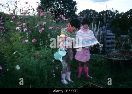 Twin cinese di bambine con innaffiatoi in alotments. Foto Stock