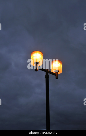 Drammatica eerie parcheggio street lampade a incandescenza twilight contro blu grigio nuvoloso cielo notturno Foto Stock