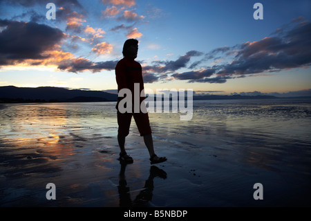 Donna che cammina lungo la spiaggia al tramonto Pohara spiaggia vicino Takaka Golden Bay Nelson regione Isola del Sud della Nuova Zelanda Foto Stock