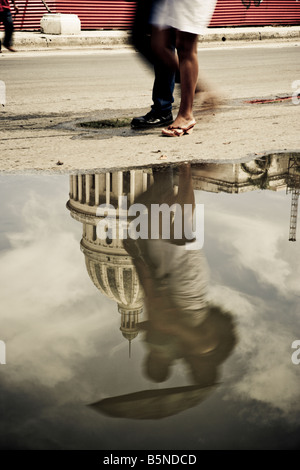 Walkers riflesso in una pozza di pioggia a piedi passato il Capitolio all Avana Vecchia Cuba Foto Stock